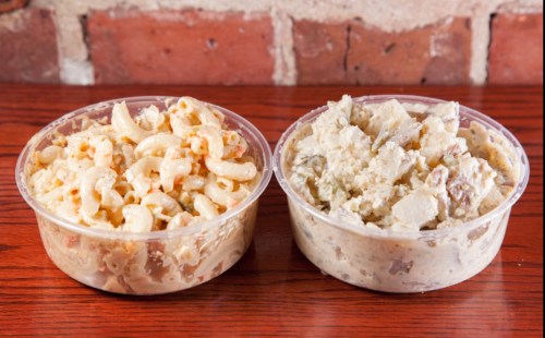 Two clear containers of pasta salad: one with macaroni and creamy dressing, the other with a chunky potato salad.