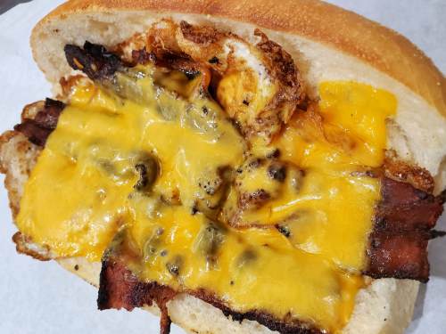 A close-up of a sandwich with crispy bacon, melted cheddar cheese, and a fried egg on a soft bread roll.