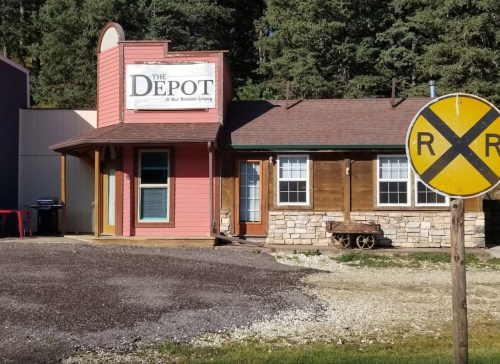 A quaint building named "The Depot" with a mix of wood and stone, surrounded by trees and a railroad crossing sign.