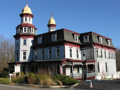 Victorian-style building with two towers, red trim, and a porch, set against a clear blue sky.