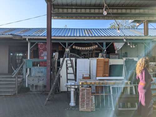 A rustic storefront filled with various vintage items, including doors, ladders, and furniture, under a blue sky.