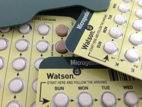 Close-up of birth control pill packs with days of the week labeled, featuring white and brown pills.