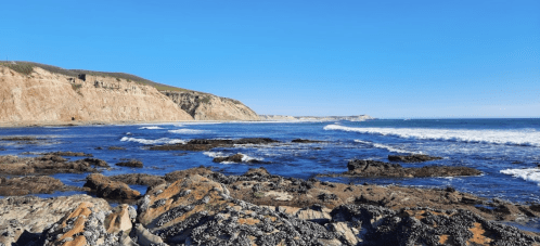 A scenic coastal view with rocky shorelines, gentle waves, and clear blue skies.