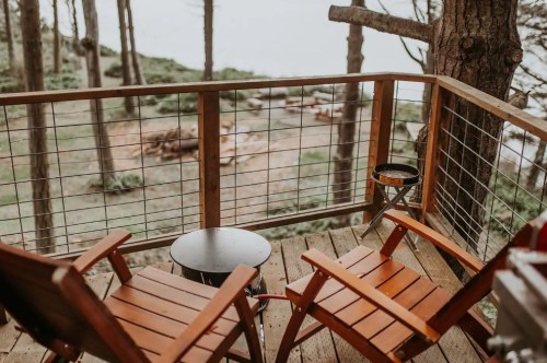 A cozy wooden balcony with two chairs overlooking a serene forest and water view.