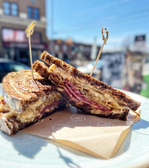 A close-up of a sliced sandwich with layers of meat and sauerkraut, held together with toothpicks on a plate.