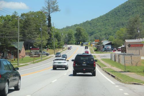 A scenic highway with cars driving, surrounded by green hills and small businesses along the roadside.