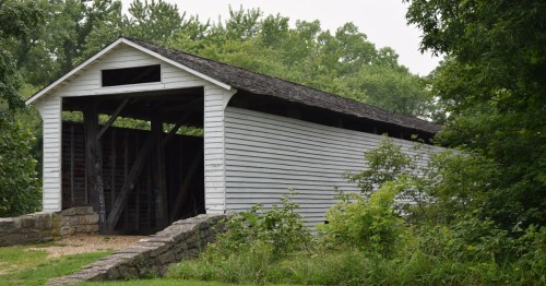 Wide shot of the historic white Union Covered Bridge surrounded by lush green trees in Paris, Missouri.