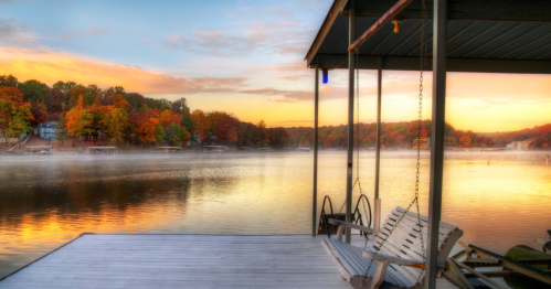 A serene lakeside view at sunset, with colorful autumn trees and a misty reflection on the water.