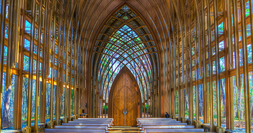 A stunning wooden chapel interior with tall, arched ceilings and large windows, surrounded by trees.