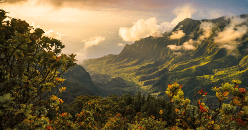 A breathtaking mountain landscape at sunset, with lush greenery and clouds hovering over the peaks.