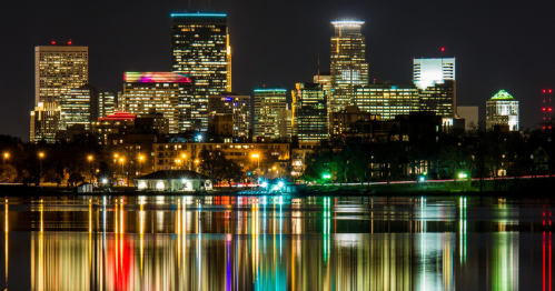 City skyline at night with colorful lights reflecting on a calm lake.