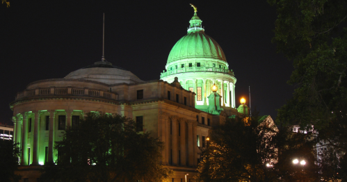 A historic building with a green-lit dome at night, surrounded by trees and city lights.