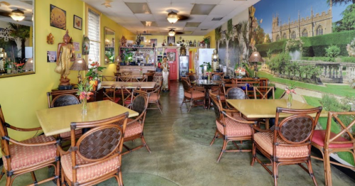 Cozy restaurant interior with yellow walls, wooden tables, and a mural of a garden. Decor includes plants and artwork.