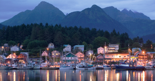 A serene harbor at dusk, with fishing boats docked and mountains rising in the background, illuminated by soft lights.