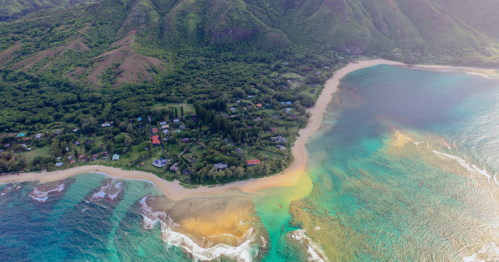 Aerial view of a coastal area with lush green hills, sandy beach, and clear turquoise waters.
