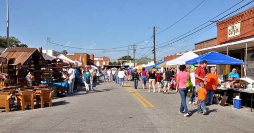 A bustling street market with vendors, colorful tents, and crowds of people enjoying the sunny day.