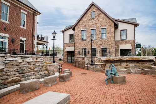 A charming stone building with a patio, surrounded by brick pathways and a small sculpture in a landscaped area.