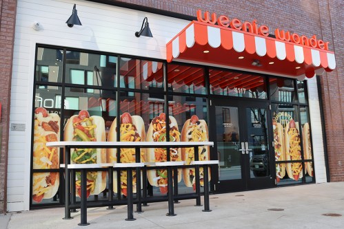 Exterior of "Weenie Wonder" restaurant featuring large hot dog graphics on the windows and a striped awning.
