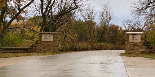 Entrance to Lake Anowabi State Park, featuring stone pillars and a paved path surrounded by autumn trees.