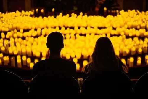 Two silhouettes sit in front of a sea of glowing candles, creating a warm and serene atmosphere.