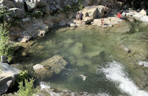 A serene natural pool surrounded by rocks, with people enjoying the water on a sunny day.