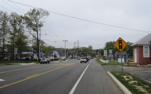 A view of a road with traffic, a stoplight ahead, and businesses lining the street under a cloudy sky.