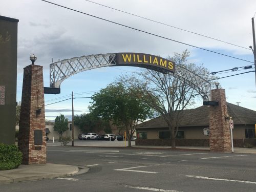 Archway sign reading "WILLIAMS" over a street, with trees and buildings in the background.