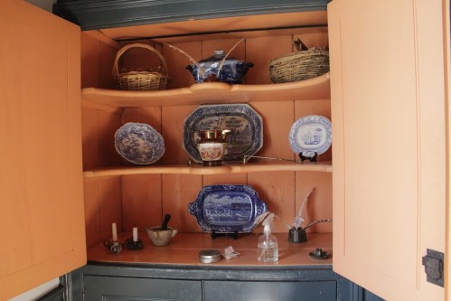 A wooden cabinet with shelves displaying various decorative plates, baskets, and vintage items.