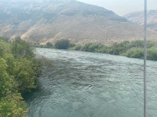 A serene river flows through a landscape of hills and greenery under a hazy sky.