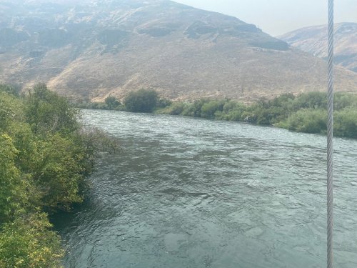A serene river flows through a landscape of hills and greenery under a hazy sky.