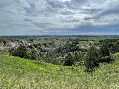 A scenic landscape featuring rolling hills, lush greenery, and a cloudy sky in the background.