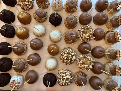 A variety of chocolate-covered caramel apples, topped with sprinkles, nuts, and popcorn, arranged neatly on a tray.