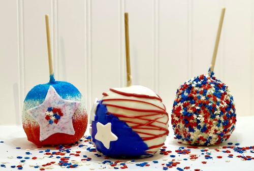 Three decorated caramel apples in red, white, and blue, adorned with sprinkles and star designs, on a white background.
