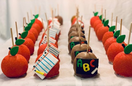 Colorful candy apples decorated as red apples and school-themed designs, arranged in neat rows on a white background.