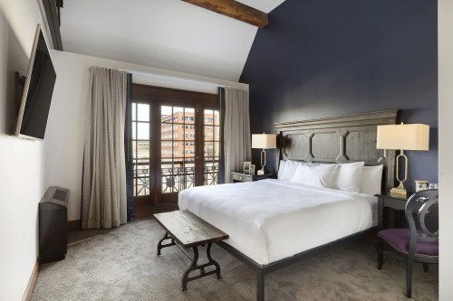 Cozy hotel room with a king bed, wooden accents, large windows, and a stylish seating area.
