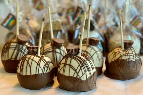Chocolate-covered caramel apples with decorative drizzles and sticks, arranged in a festive display.