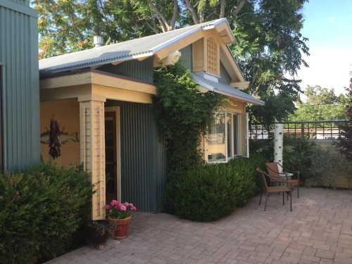 A charming house with green siding, a porch, and potted plants, surrounded by trees and a brick patio.