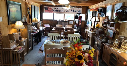 Cozy interior of a rustic shop featuring wooden furniture, decor, and a banner reading "Solid Wood American Made."