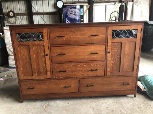 A wooden dresser with multiple drawers and decorative glass panels, set in a garage or workshop environment.