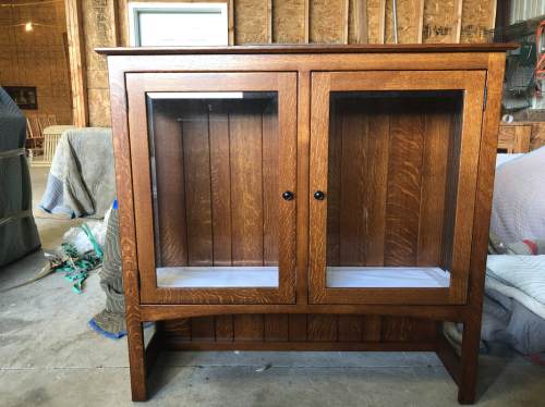 A wooden display cabinet with glass doors, featuring a rich brown finish and a curved base, set in a workshop.