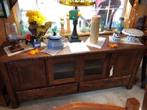 A wooden sideboard with glass doors, decorated with blue and white ceramics, a lamp, and autumn leaves.
