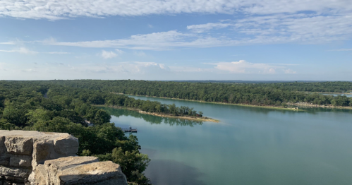 A serene view of a river winding through lush green trees under a blue sky with scattered clouds.