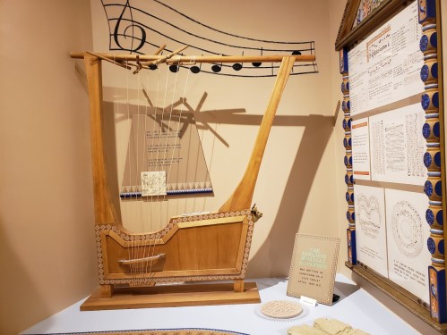 A wooden string instrument displayed in a museum, with musical notes and educational materials in the background.