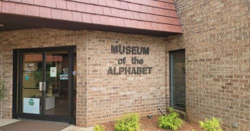 Entrance to the Museum of the Alphabet, featuring a brick facade and large sign. The door is open.