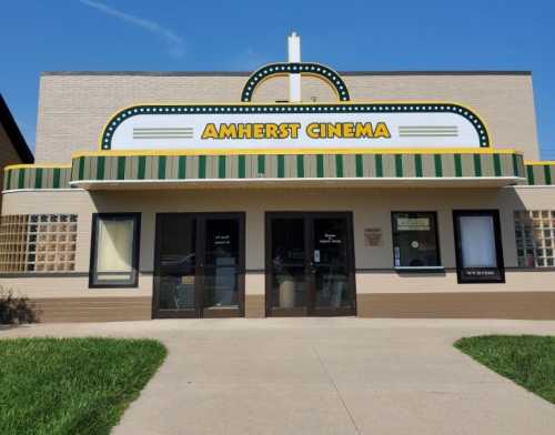 Front view of Amherst Cinema, featuring a marquee and green striped awning, set against a clear blue sky.