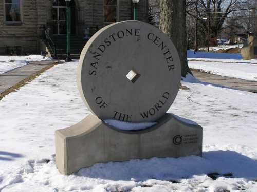 A large stone monument inscribed with "Sandstone Center of the World," surrounded by snow.