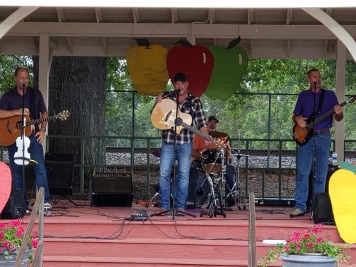 A band performs on stage with guitars and drums, surrounded by colorful decorations and flowers.