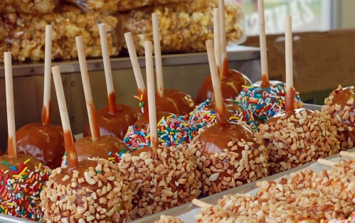 A display of caramel apples coated in nuts and sprinkles, with wooden sticks, set against a backdrop of popcorn.