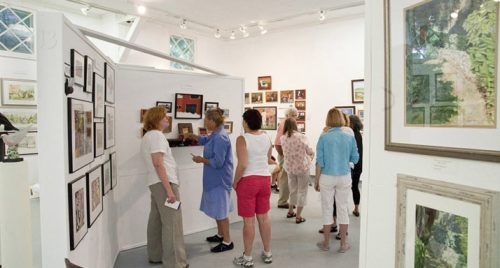 A group of people viewing artwork in a gallery, surrounded by framed paintings and photographs on the walls.