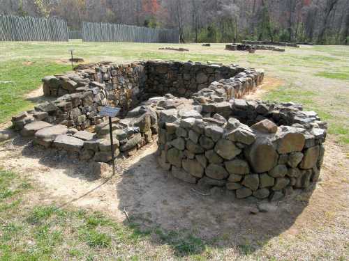 Stone ruins of a circular structure, surrounded by grassy area, with informational signs nearby.